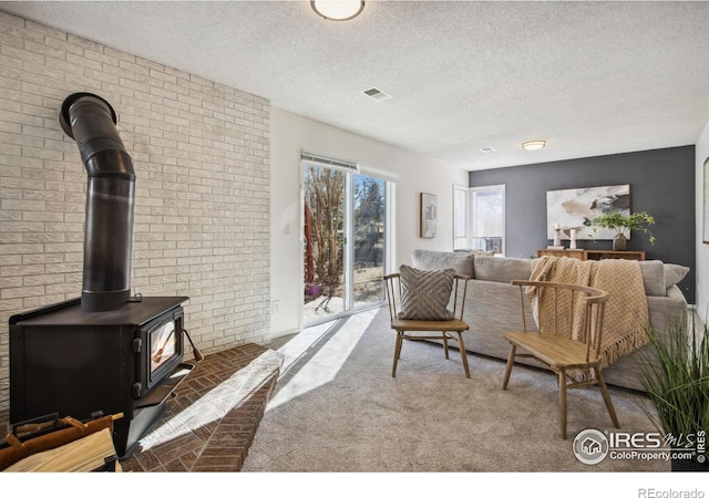 living area featuring a wood stove, carpet floors, visible vents, and a textured ceiling