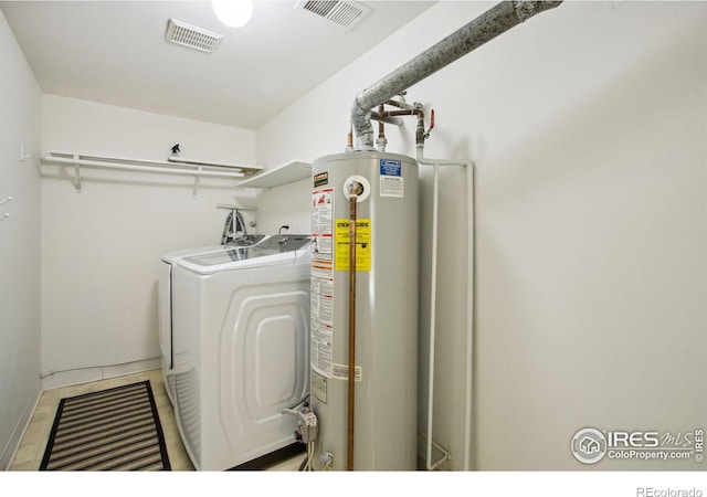 clothes washing area featuring visible vents, laundry area, water heater, and washer and clothes dryer