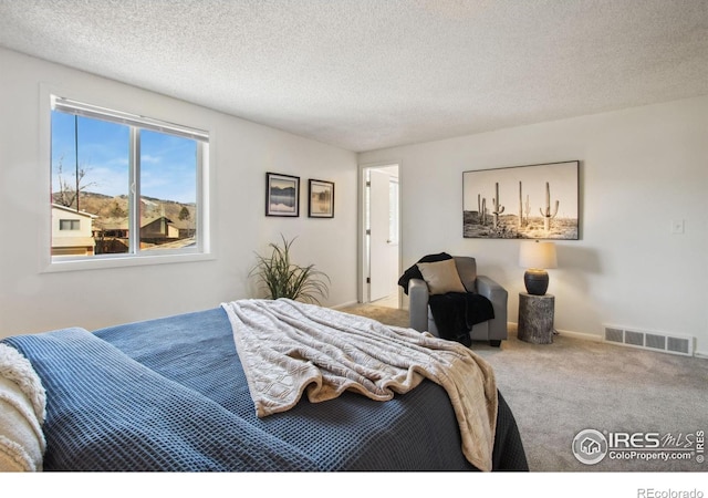 carpeted bedroom featuring a textured ceiling, visible vents, and baseboards