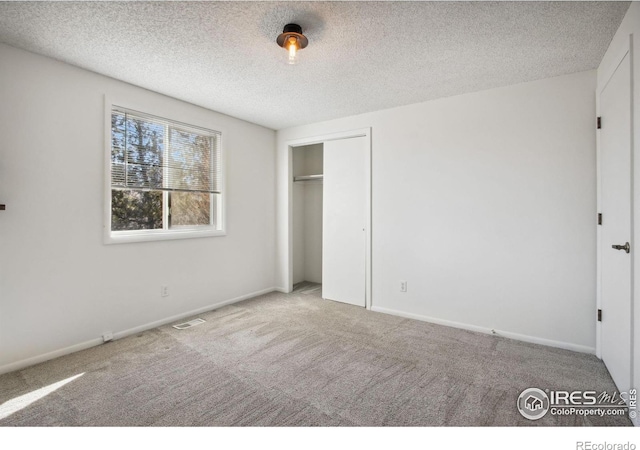 unfurnished bedroom featuring carpet floors, a closet, visible vents, a textured ceiling, and baseboards