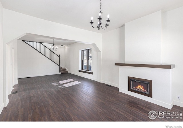 unfurnished living room with dark wood-style floors, a warm lit fireplace, a notable chandelier, and stairs