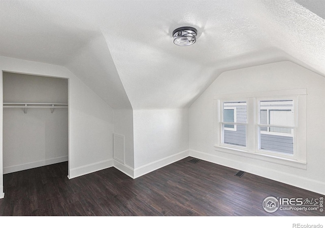 bonus room featuring dark wood-style flooring, vaulted ceiling, a textured ceiling, and baseboards