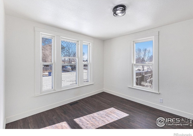 unfurnished room with baseboards, visible vents, dark wood finished floors, and a textured ceiling