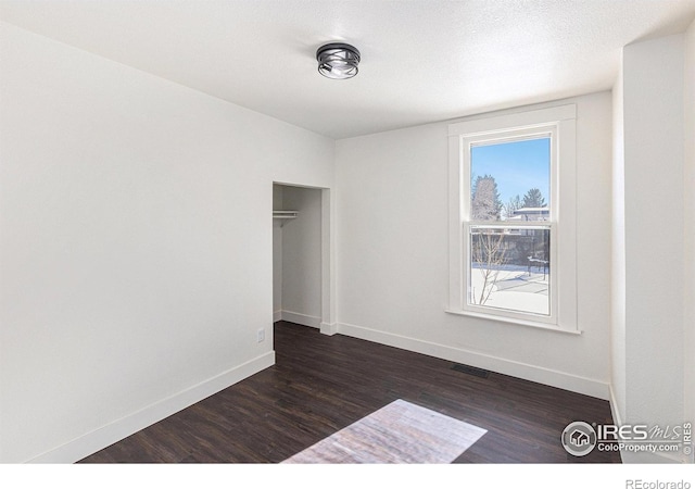 spare room featuring dark wood-style floors, visible vents, a textured ceiling, and baseboards