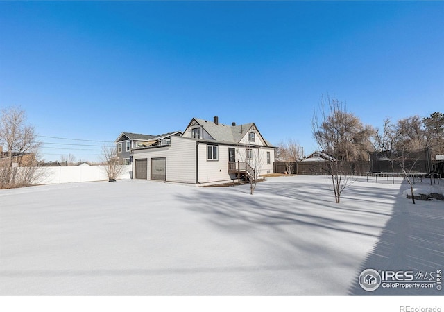 snow covered property with a garage, a trampoline, and fence