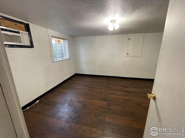 below grade area with dark wood-style floors, a textured ceiling, a wall unit AC, and baseboards