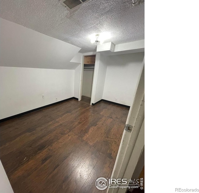 bonus room featuring a textured ceiling, dark wood-type flooring, visible vents, baseboards, and vaulted ceiling