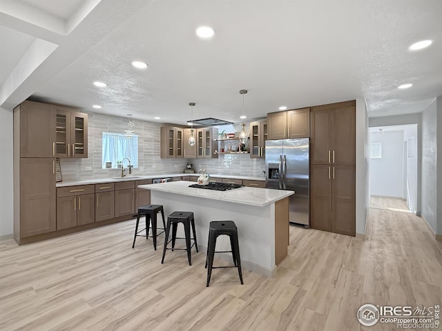 kitchen featuring a breakfast bar area, black gas cooktop, light wood-type flooring, stainless steel refrigerator with ice dispenser, and a sink