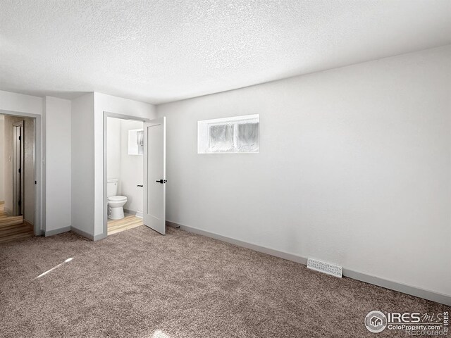 unfurnished bedroom featuring visible vents, carpet flooring, connected bathroom, a textured ceiling, and baseboards