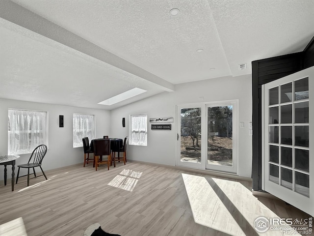 home office with a textured ceiling, vaulted ceiling with skylight, wood finished floors, and visible vents