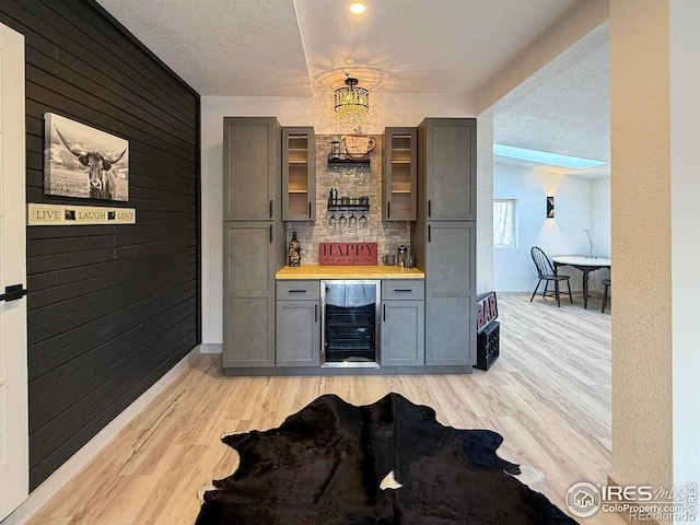 bar with light wood-style flooring, wood walls, a textured ceiling, a bar, and beverage cooler