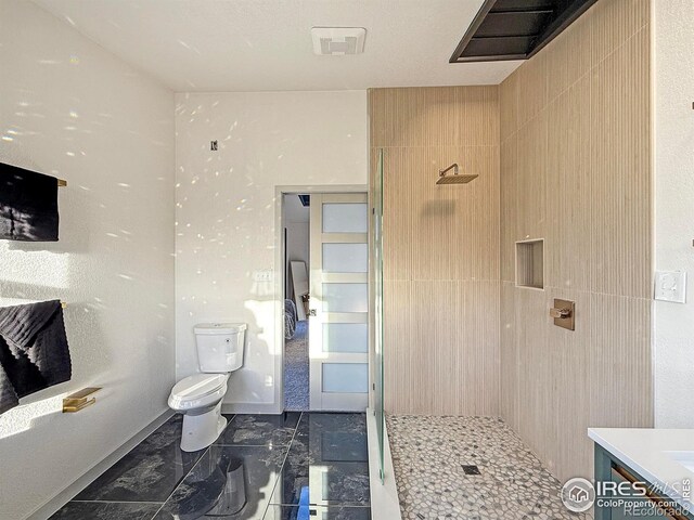 bathroom featuring toilet, vanity, baseboards, marble finish floor, and tiled shower