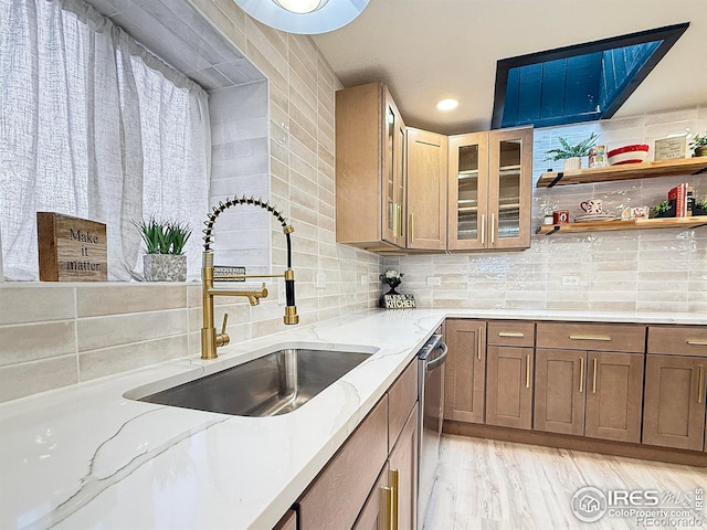 kitchen with stainless steel dishwasher, backsplash, a sink, and light stone counters