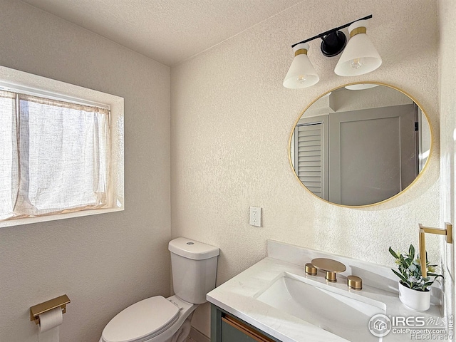 half bath with a textured ceiling, a textured wall, vanity, and toilet