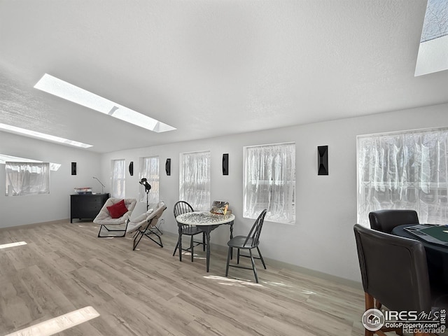 dining room featuring vaulted ceiling with skylight, a textured ceiling, and wood finished floors