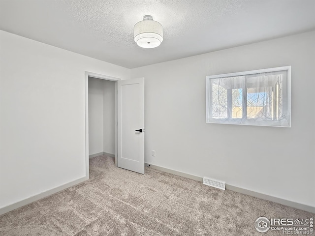 unfurnished bedroom featuring carpet, a textured ceiling, visible vents, and baseboards