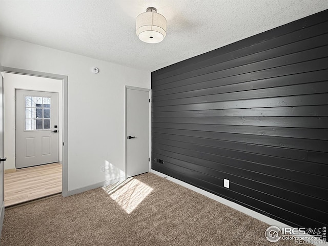 carpeted empty room with a textured ceiling and wood walls