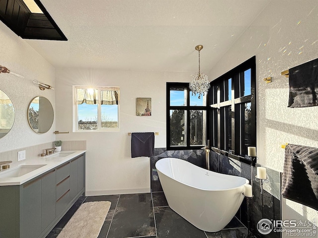 bathroom with a chandelier, a soaking tub, a sink, and a textured ceiling