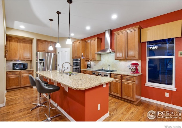 2185 Diamond Creek Dr, Colorado Springs, CO 80921 - kitchen featuring wall chimney exhaust hood, stainless steel appliances, light wood-style floors, an island with sink, and a kitchen breakfast bar