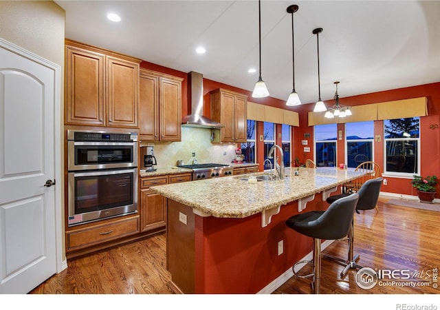 2185 Diamond Creek Dr, Colorado Springs, CO 80921 - kitchen with a breakfast bar area, a sink, appliances with stainless steel finishes, wall chimney exhaust hood, and a center island with sink