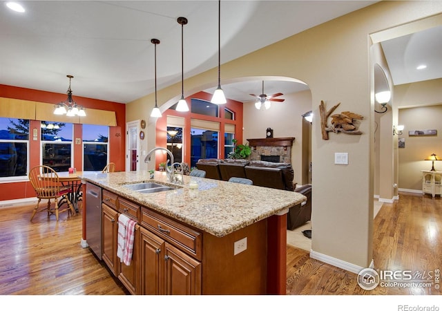 2185 Diamond Creek Dr, Colorado Springs, CO 80921 - kitchen featuring arched walkways, a center island with sink, hanging light fixtures, a sink, and light wood-type flooring