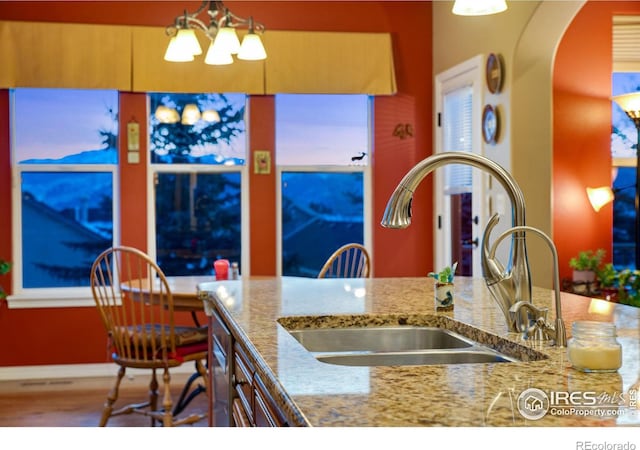 2185 Diamond Creek Dr, Colorado Springs, CO 80921 - kitchen featuring arched walkways, light stone counters, hanging light fixtures, a chandelier, and a sink