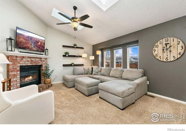 living room with a ceiling fan, a brick fireplace, light carpet, vaulted ceiling with skylight, and baseboards