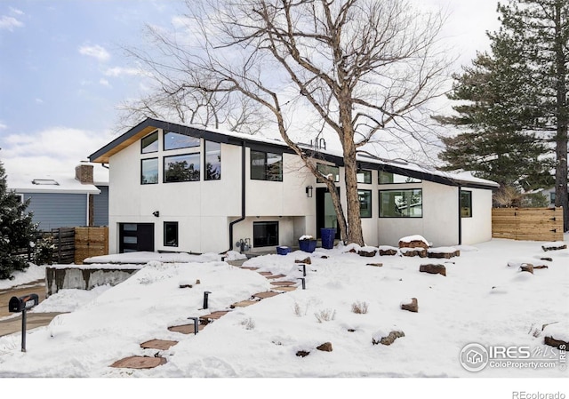 snow covered house featuring fence and stucco siding