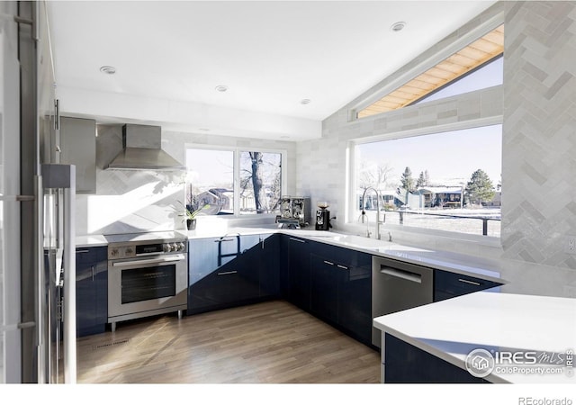 kitchen featuring stainless steel appliances, light countertops, vaulted ceiling, and wall chimney range hood