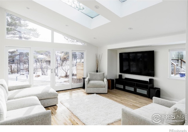 living room with vaulted ceiling with skylight, french doors, and light wood-style flooring