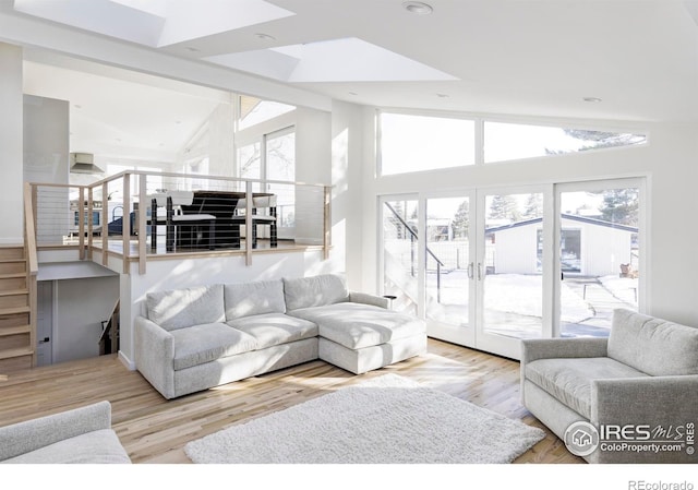 living area featuring stairs, high vaulted ceiling, french doors, and light wood-type flooring