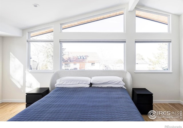 bedroom featuring vaulted ceiling with beams, multiple windows, wood finished floors, and baseboards