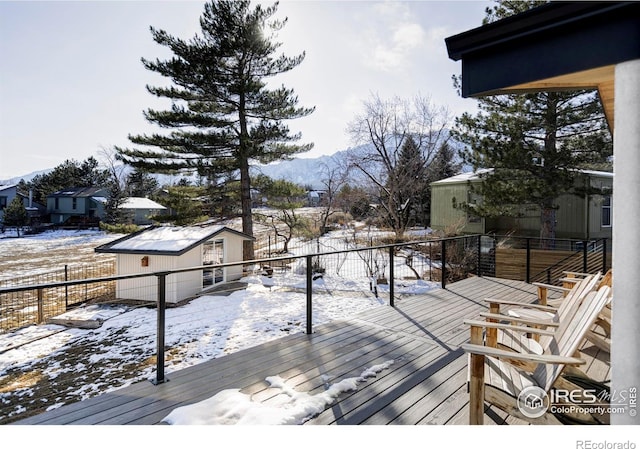 snow covered deck with an outbuilding, a mountain view, and fence