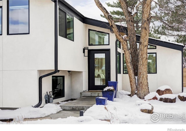 snow covered property entrance featuring stucco siding