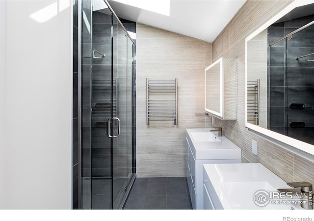 bathroom featuring tile walls, lofted ceiling, a stall shower, a sink, and tile patterned flooring