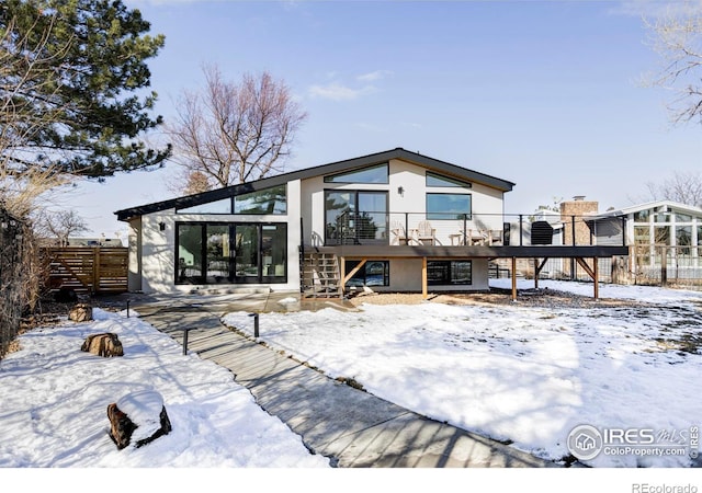 snow covered rear of property with stairway, fence, a wooden deck, and stucco siding