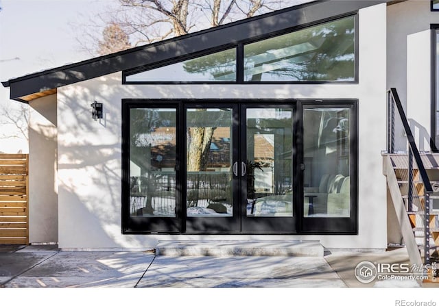 view of exterior entry featuring fence, french doors, and stucco siding