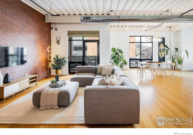 living area with a healthy amount of sunlight, a notable chandelier, brick wall, and wood finished floors