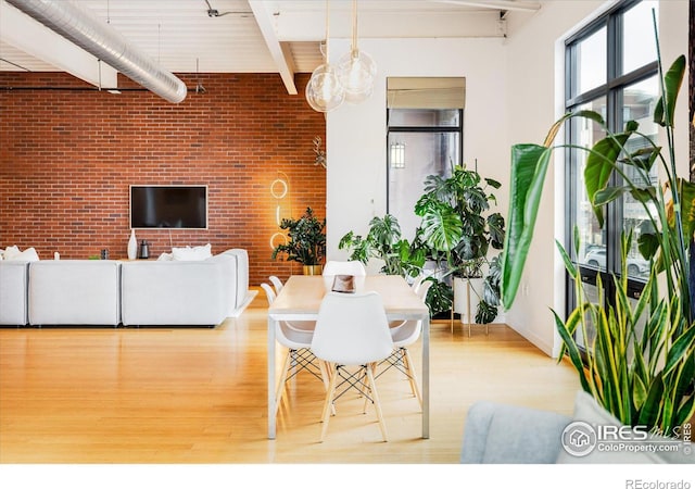 dining space featuring beamed ceiling, light wood-style flooring, and brick wall