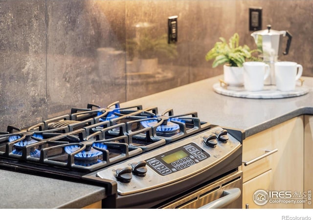 interior details with stainless steel range with gas cooktop, dark countertops, and light brown cabinetry