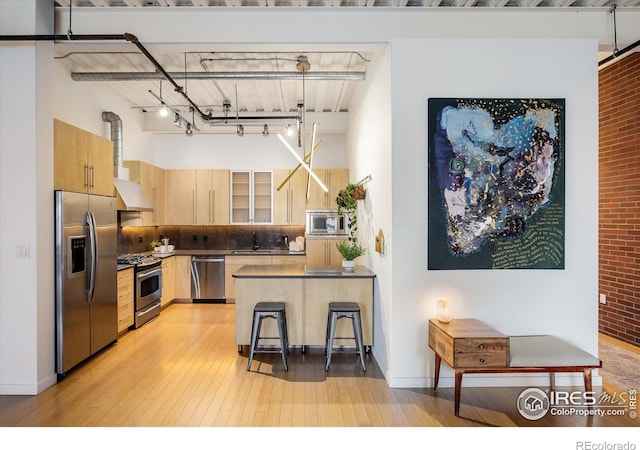 kitchen with light brown cabinets, stainless steel appliances, a kitchen breakfast bar, dark countertops, and decorative light fixtures