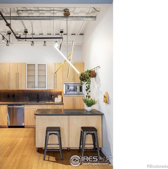 kitchen with dark countertops, a breakfast bar, stainless steel appliances, light brown cabinetry, and a sink