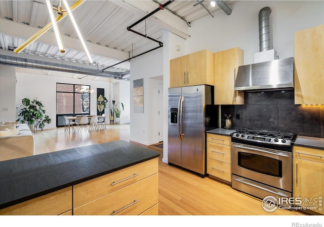 kitchen with dark countertops, wall chimney exhaust hood, tasteful backsplash, and stainless steel appliances