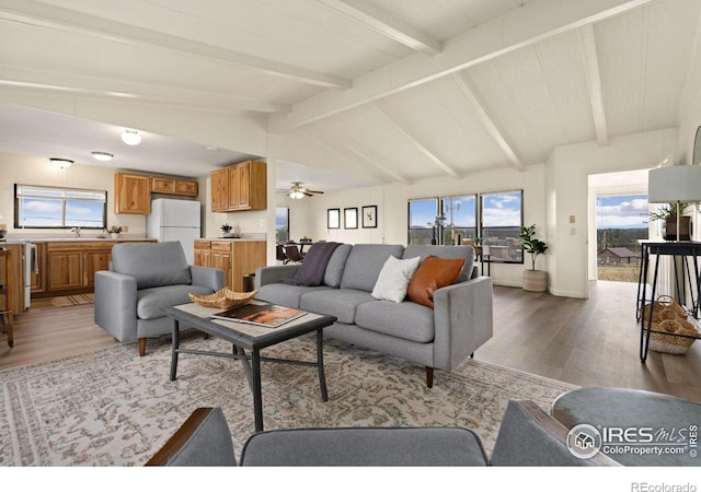 living area with vaulted ceiling with beams, light wood-style flooring, and baseboards