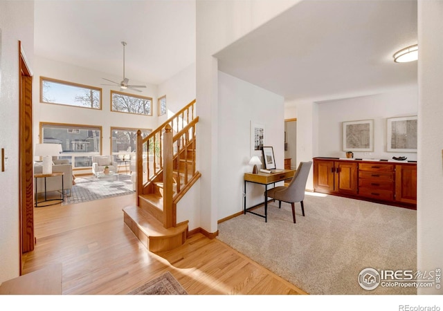 interior space with light wood finished floors, baseboards, ceiling fan, stairway, and a high ceiling