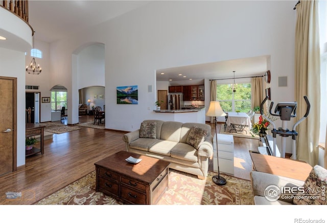 living room with a chandelier, dark wood-type flooring, plenty of natural light, and a towering ceiling