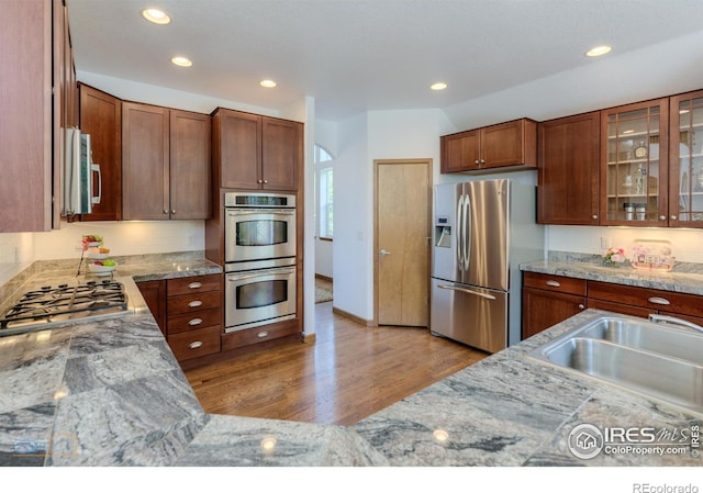 kitchen featuring glass insert cabinets, light stone countertops, appliances with stainless steel finishes, and a sink