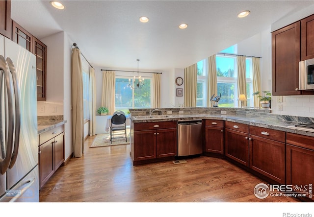 kitchen featuring tasteful backsplash, wood finished floors, hanging light fixtures, stainless steel appliances, and a sink