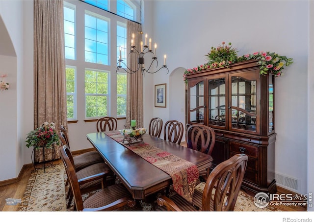 dining space featuring arched walkways, a notable chandelier, a high ceiling, visible vents, and light wood finished floors