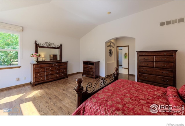 bedroom featuring lofted ceiling, arched walkways, visible vents, baseboards, and light wood-type flooring